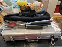 Set of barbecue utensils including tongs and spatulas on top of aluminum hard case with black soft carrying bag