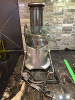 Full view of Breville juicer with transparent feeding chute and power cord on counter, silver body with protective cage at bottom.
