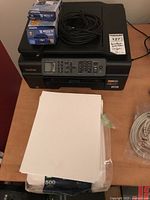 Top view of Brother Work Smart Series printer on table with two boxed LC103BK XL black ink cartridges, power cord, and stack of white printer paper visible.