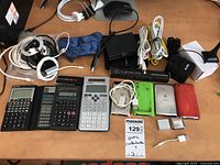 Photo showing calculators, iPods, charging cables, Lexus paint pen, Ruxin adaptor, and game controller arranged on table.