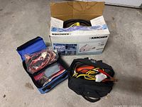 Photo showing Karcher power washer box, blue bag with jumper cables, and black bag with jumper cables and small supplies