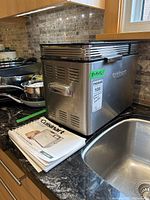 Cuisinart bread maker unit with recipe and instruction booklet placed on kitchen counter.