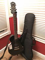 Black Epiphone Special II electric guitar and soft-sided gig bag leaning against wall