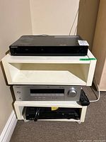 Photo of Samsung BluRay Player BD-P1500 on top shelf of white modular stand along with Yamaha receiver and Cisco cable box below.