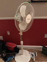 Front angle view of the white Pelonis pedestal fan showing the base, adjustable pole, and front grill with blades.