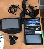 Garmin nuvi 265W GPS device with screen and accessories including car charger, mount, and case, along with a City Navigator NT map box and second GPS device visible.