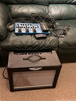 Overall lot showing Trainor amp cabinet on floor with Boss ME-50 pedalboard and cables on sofa