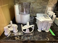 Moulinex food processor base with the mixing bowl and multiple blades and attachments laid out on a countertop.