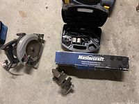 Black & Decker rotary tool in case, Mastercraft reciprocating saw with box, and metal bench clamp shown on floor.