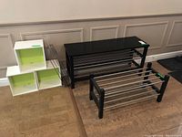 Overview of two metal and wood shoe racks, three white storage cubes with green inside, and a Salter kitchen scale, displayed on floor against wall