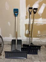 Four snow shovels, display of all showing blades and handles including blue plastic handle one and two with black handles