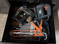 Top view of open drawer containing Black & Decker jigsaw saw, orange caulking gun, assorted wrenches and hand tools