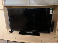 Front view of Samsung flat-screen TV with screen off, showing Samsung logo and TV stand, remote located on the stand.