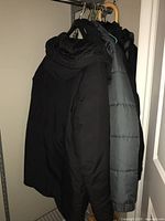 Photo of four women's coats hanging on hangers in a closet, including black and gray coats.
