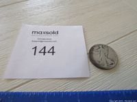 Photo of the coin next to a MaxSold lot number card for scale and identification