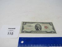 Front side of 1953 red seal $2 bill with visible serial number and ruler for scale.
