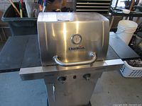 Front view of Char Broil stainless steel gas grill showing temperature gauge, lid handle, control knobs, and side shelves.