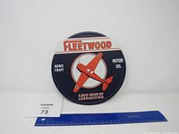 Front view of round Fleetwood metal sign featuring red airplane and advertising motor oil.