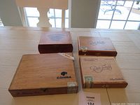 Four vintage hinged wooden cigar boxes on table, brands visible include Cohiba and Ron Jonny