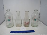 Four vintage milk bottles displayed together on white background with blue ruler for scale.