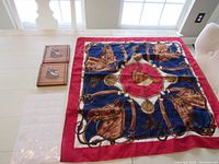 Silk flag with horse and equestrian gear design laid flat on table, alongside two wooden dog plaques.
