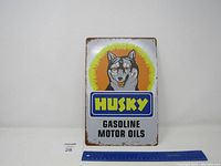 Metal sign showing Husky logo with a yellow halo background and text 'HUSKY GASOLINE MOTOR OILS'. Rust and wear visible on edges.