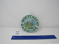 Front view of the round 'Independent Gasoline' metal sign with three drummers illustration and a ruler for scale.