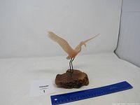 Overall view of pink flamingo sculpture on wooden base with ruler for scale