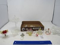 Photo showing multiple glass items laid out including bowls, candy dishes, and figurines such as birds and an angel.