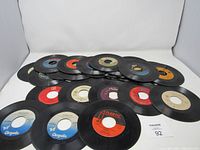 Photo showing 18 45 RPM vinyl records arranged in two rows with various label colors and wear.