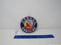 Full view of the round metal sign with ruler for size reference, showing Oregon Gasoline Chief branding and colors.