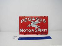 Front view of the Pegasus Motor Spirit red metal sign, showing logo, text and ruler for scale.