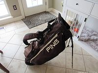 Full view of the brown Ping standup golf bag angled to show shape and structure including the attached stand.