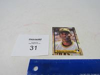 Baseball card of Roberto Clemente in Pirates uniform with MaxSold lot number and ruler for size reference.