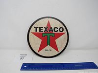 Front view of the Texaco metal round sign with visible scratches and wear, next to a ruler showing approximate size.