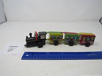 Full side view of the tin metal wind-up train showing black engine and three colorful passenger cars with characters.