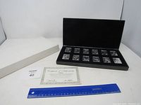 View of all 12 silver-tone embossed metal baseball cards arranged in a black velvet-lined presentation box with certificate of authenticity and ruler for scale.