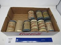 Photo of nine vintage Edison rolls in cardboard box with ruler for scale