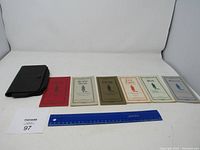 Photo showing six vintage books with different colored covers side by side on a white background alongside a blue ruler for scale.
