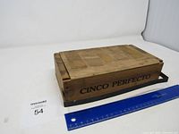 Full view of the closed wooden box with 'CINCO PERFECTO' printed on the side and a blue ruler alongside for scale.