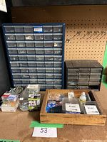 View of blue and black multi-drawer organizers filled with various nuts, bolts, screws and small hardware items, plus boxed screws and bolts, and a wooden tray with additional hardware items and small accessories.