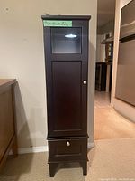 Front view of the tall dark wood bathroom storage cabinet showing glass panel and drawer