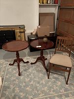 Two wooden side tables with scalloped edges paired closely, wooden folding chair with beige cushioned seat, placed on floral area rug.