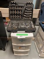 Full closed look of the socket wrench set in open hard plastic case on top of the plastic drawer storage unit in the tool room.