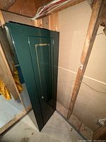 Green Stack-On firearm cabinet standing upright against unfinished wall and floor, showing side and front angles.