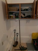 Corner view showing wall cabinet with gardening supplies, and three garden tools plus electric hedge trimmer below.