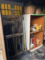 General view of garden and cleaning tools stored in wooden racks inside a shed with yellow window panes.