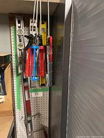 Lot showing mounted metal spirit levels and manual caulking guns hanging on pegboard.