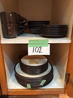 Wide cabinet shot showing stacked cups, bowls, and plates with green tape marks on chipped items.