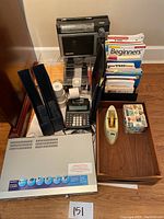 Photo showing office supplies including magazine holders, calculator, rolls of tape, black radio, books, clear acrylic organizer, wooden tray with tape dispenser and cube puzzle, and Sony DVD/VHS player on the floor.